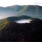 Eine neblige Landschaft mit einem nebelverhangenen See in einer Senke, umgeben von grünen Bergen.