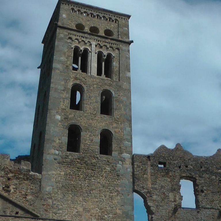Ein hoher Steinturm mit Zinnen und angrenzende historische Mauern vor einem blauen Himmel.