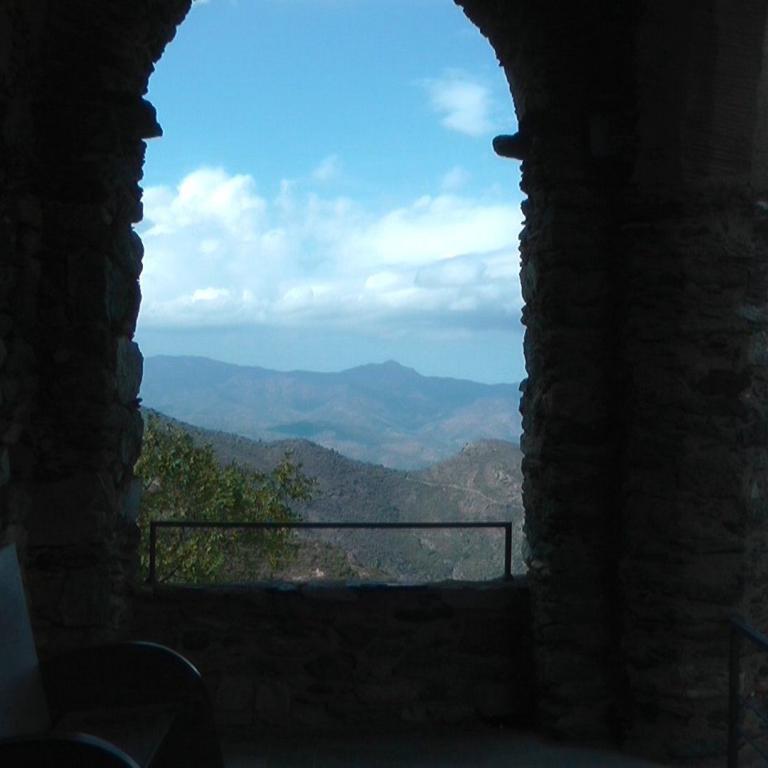 Ein Panoramablick durch einen steinernen Durchgang auf eine Bergkette und das Meer.