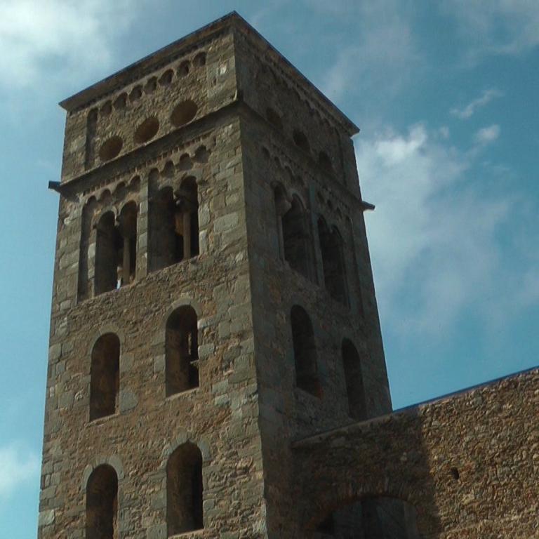 Ein hoher, steinernes Turm der Ruine, umrahmt von niedrigeren Mauerresten, vor einem Wolkenhimmel.