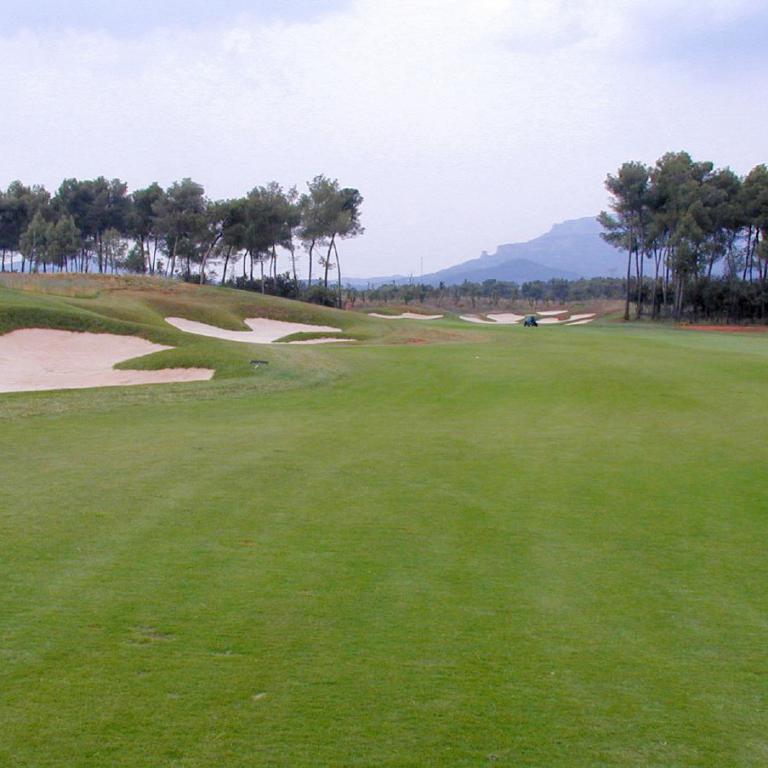 Weitwinkelaufnahme eines Golfplatzes mit ausgeprägtem Rasen, Sandbunker und Waldhintergrund.